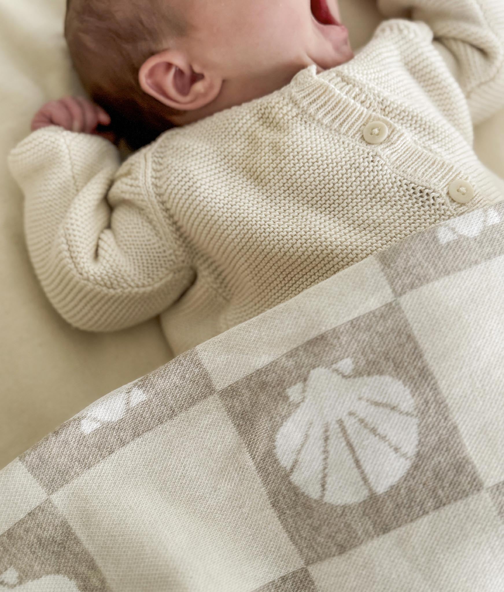 Newborn baby wearing a cream knitted sweater lying on a patterned blanket.