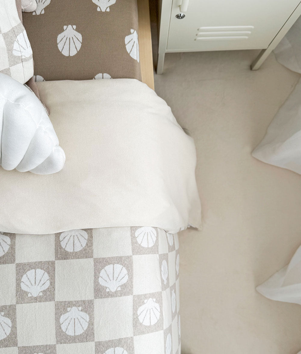 Bed with shell-patterned bedding and headboard, white cabinet in the background