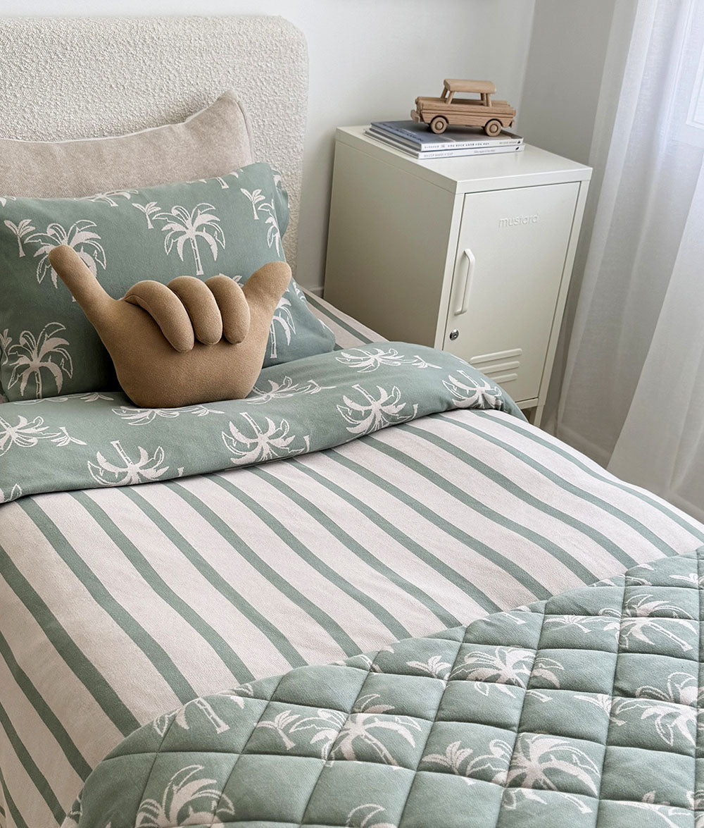 Bed with green and white striped bedding and palm leaf patterned pillows.