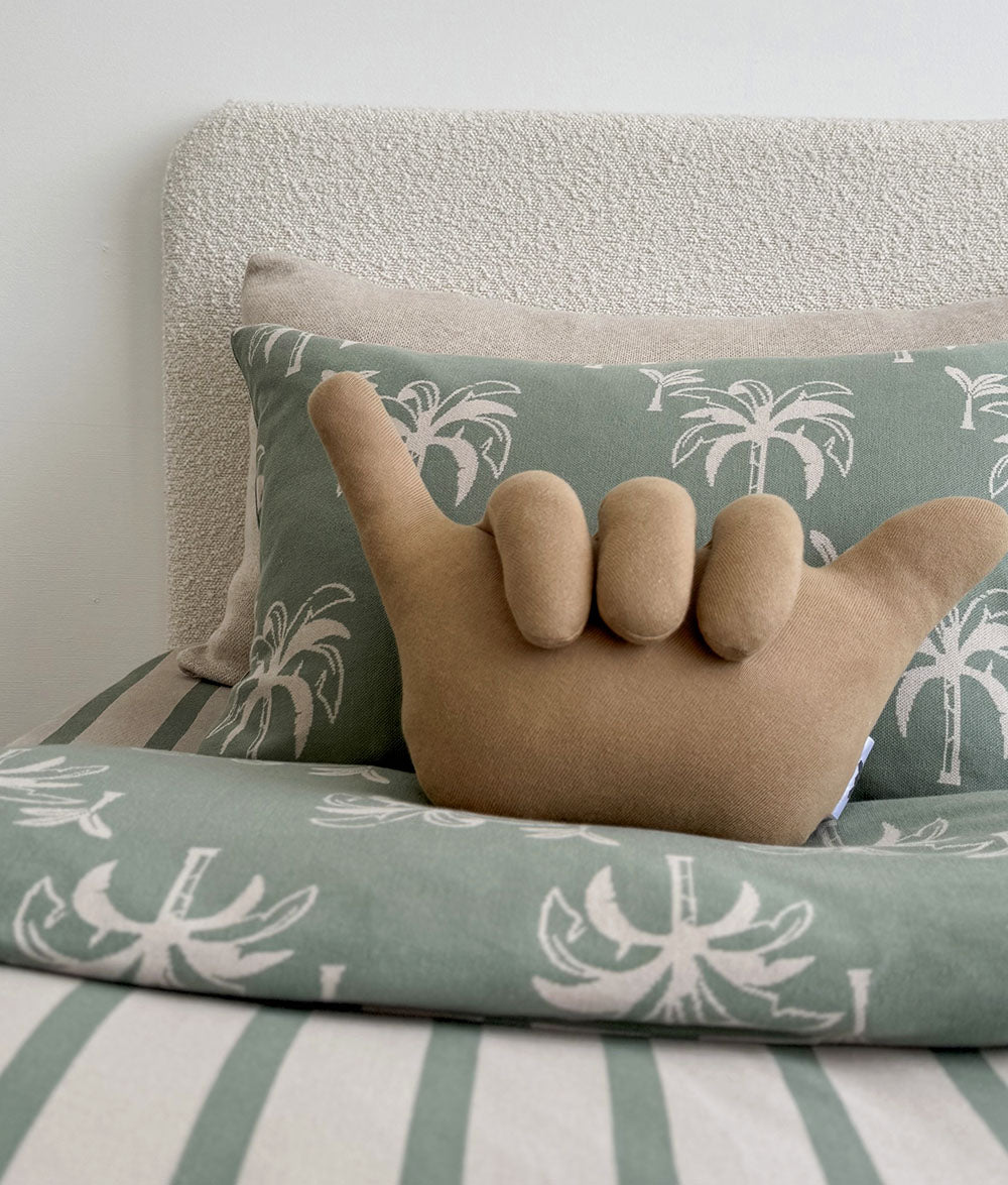 Decorative pillow with palm tree pattern on a couch with a hand-shaped pillow on top.