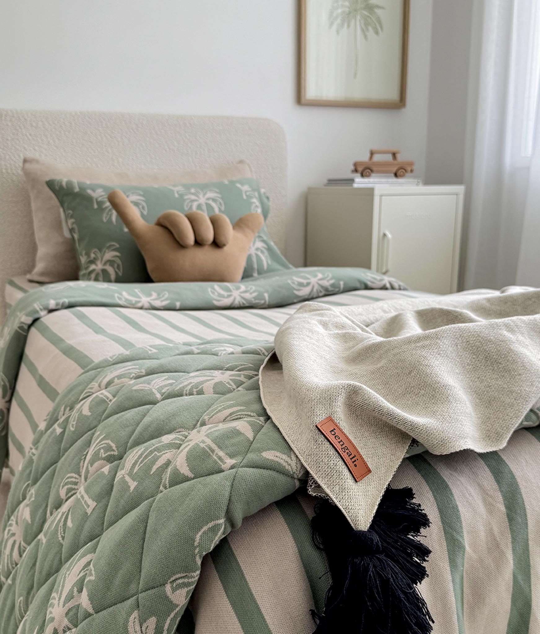 Bed with green and beige quilt, decorative pillow, and blanket in a bedroom setting.