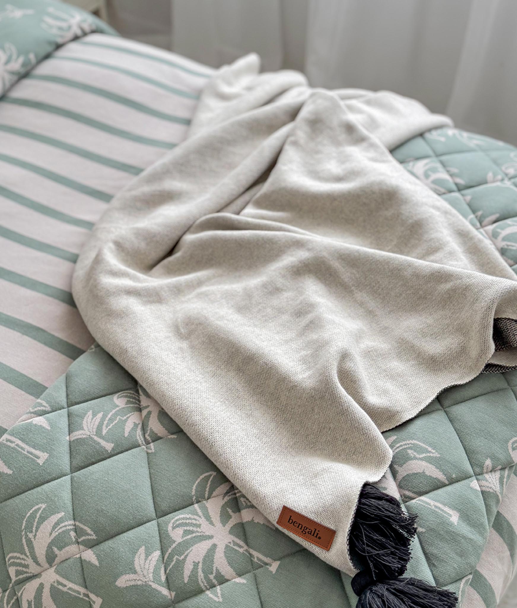 Beige blanket with a brand label on a bed with a palm tree pattern