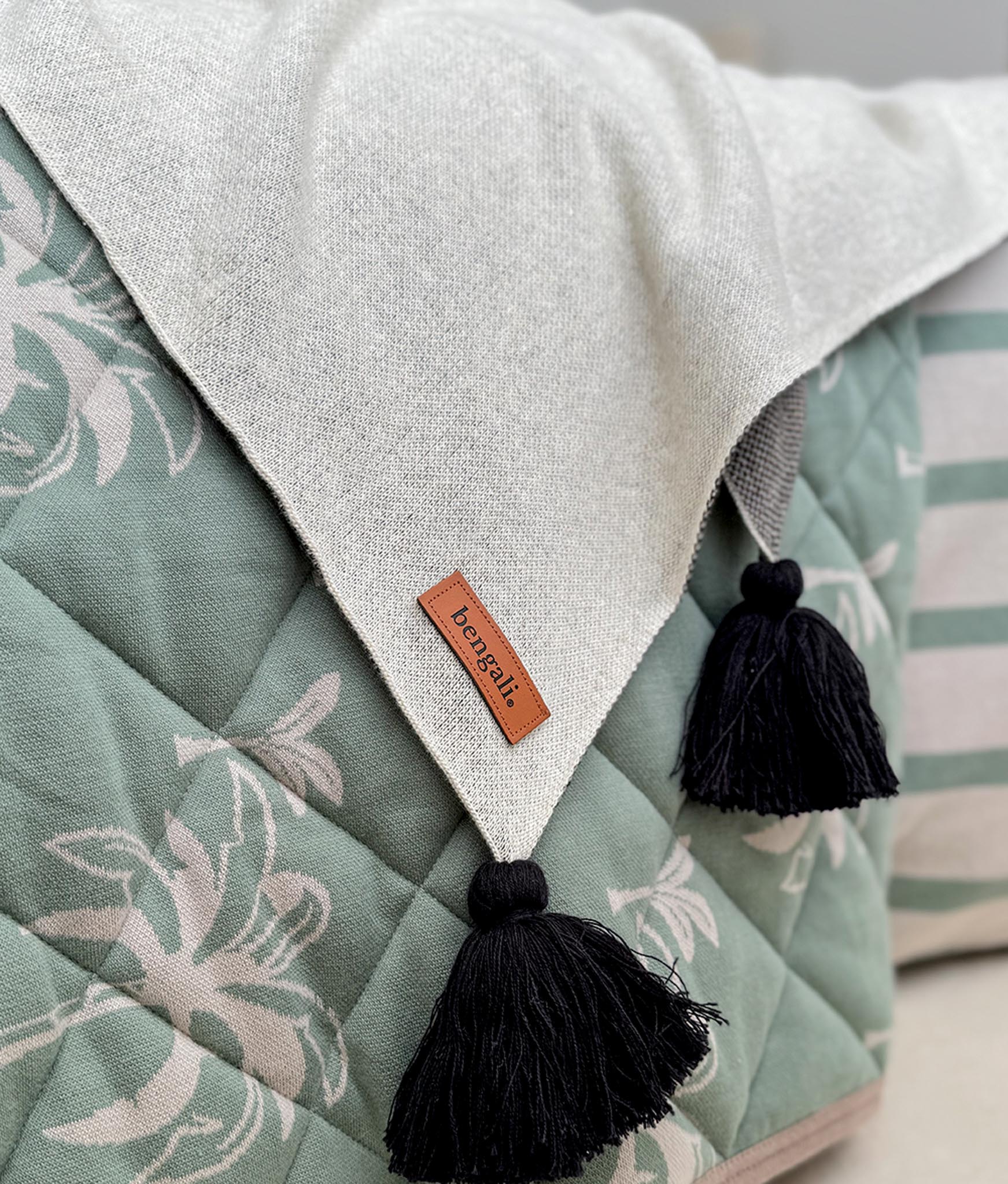 Light beige blanket with black tassels on a green floral cushion, featuring the brand 'Bengali'.