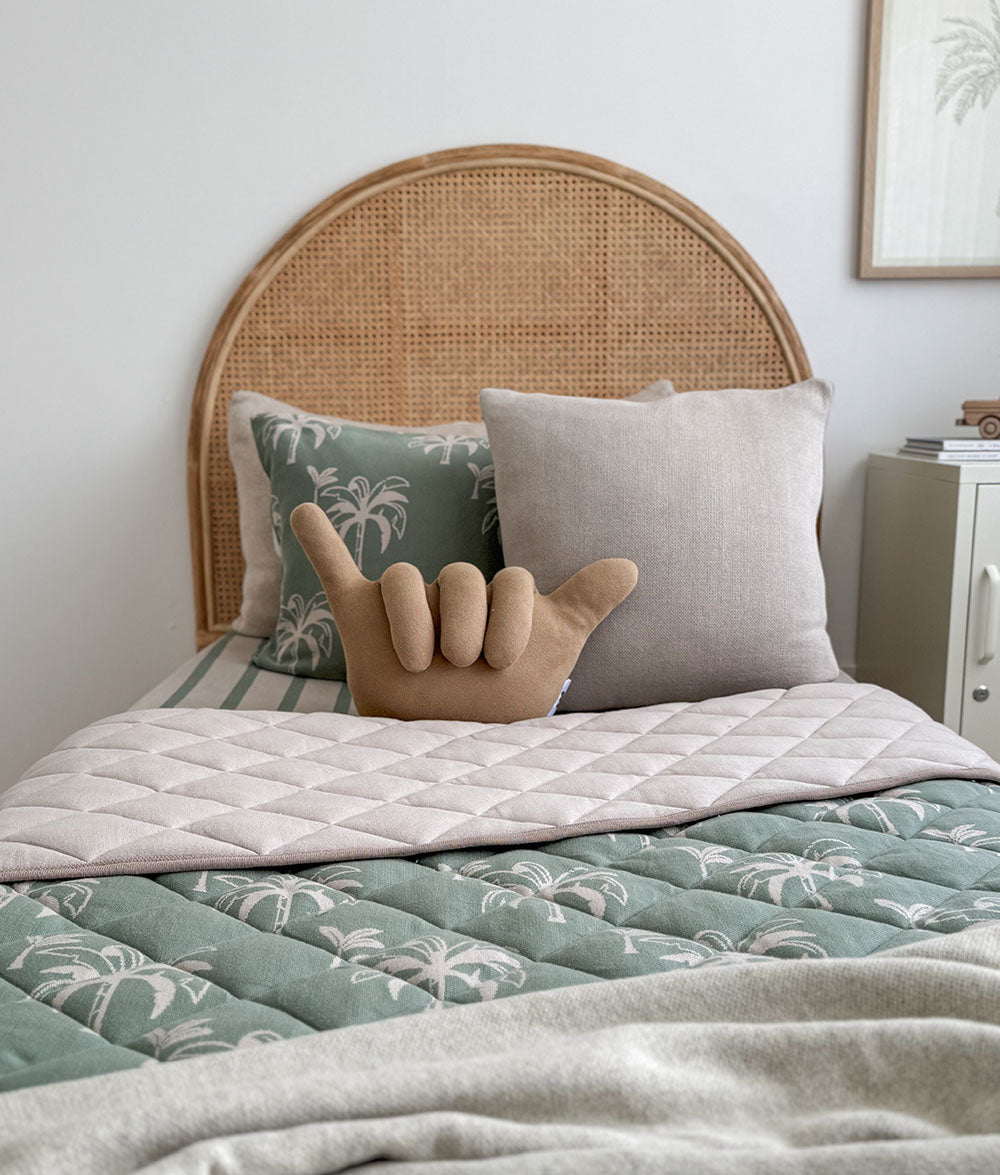 Bed with wicker headboard, palm tree patterned bedding, and decorative pillow.