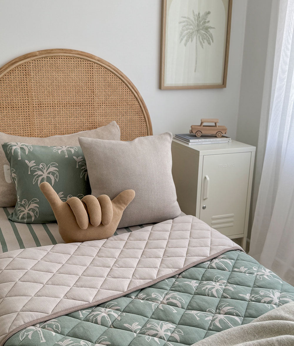 Bedroom with a bed featuring a wicker headboard, palm tree-patterned bedding, and decorative pillows.