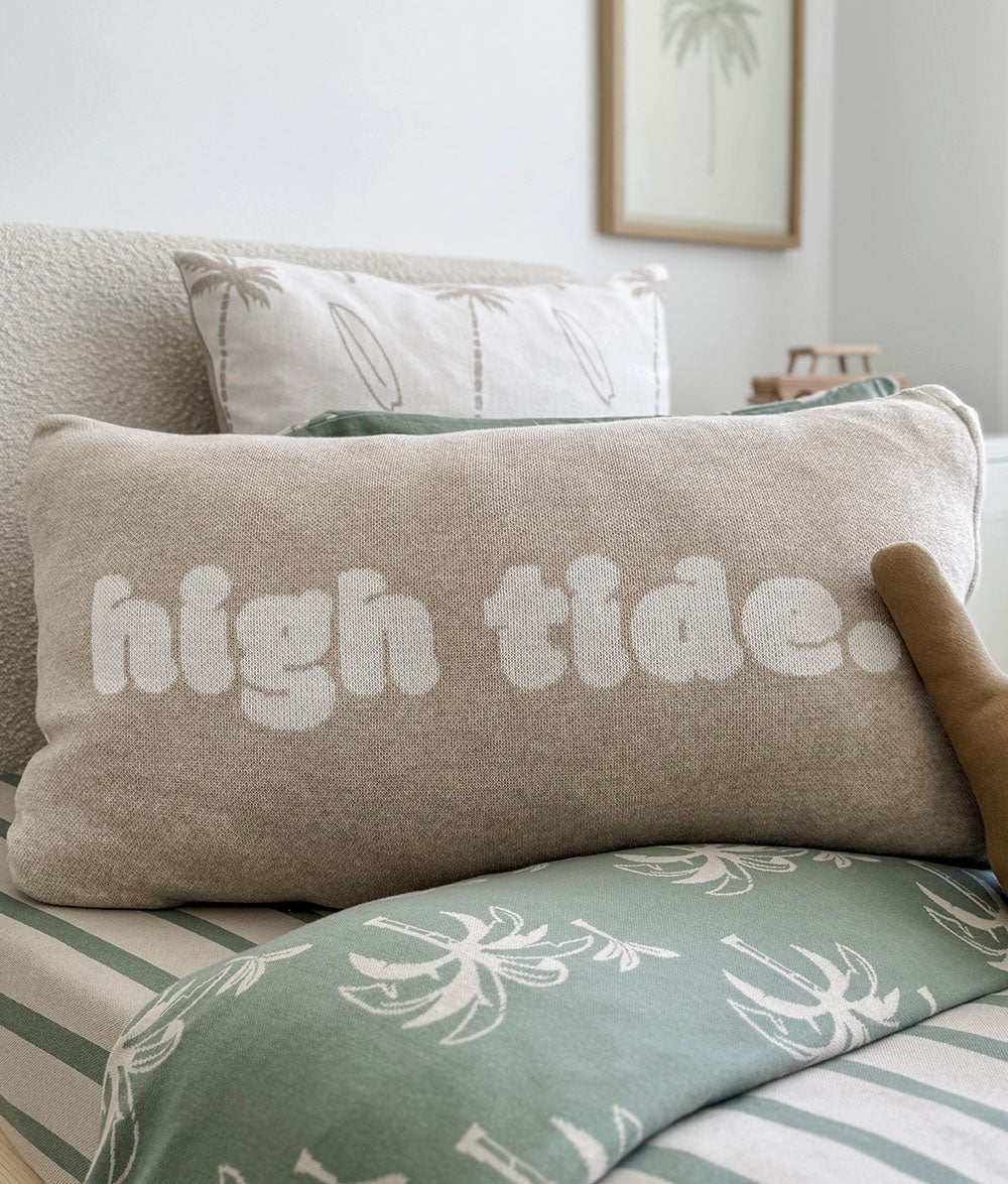 Beige pillow with 'high tide' text on a bed with green and white bedding.