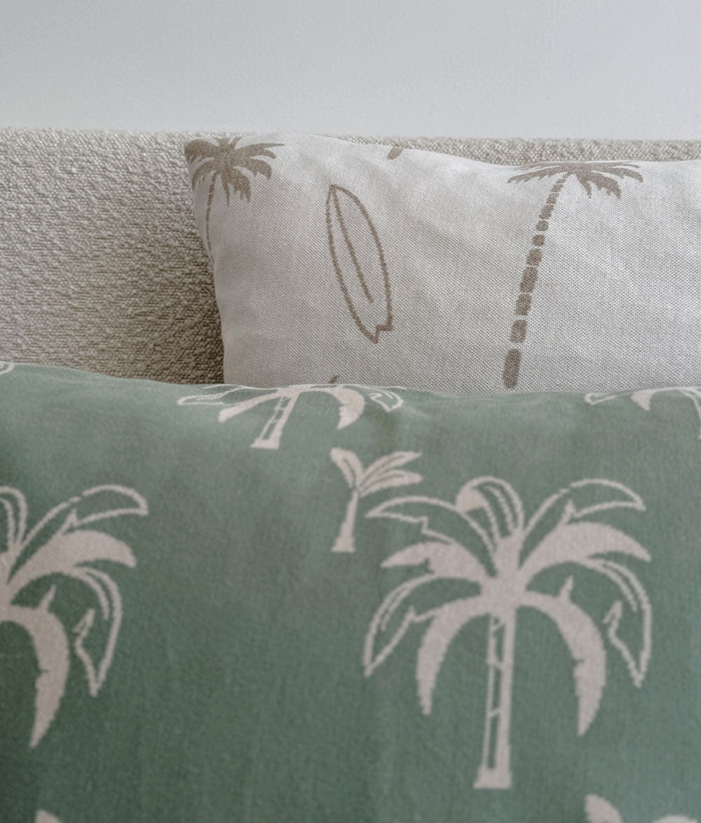 Two cushions with palm tree patterns on a neutral background