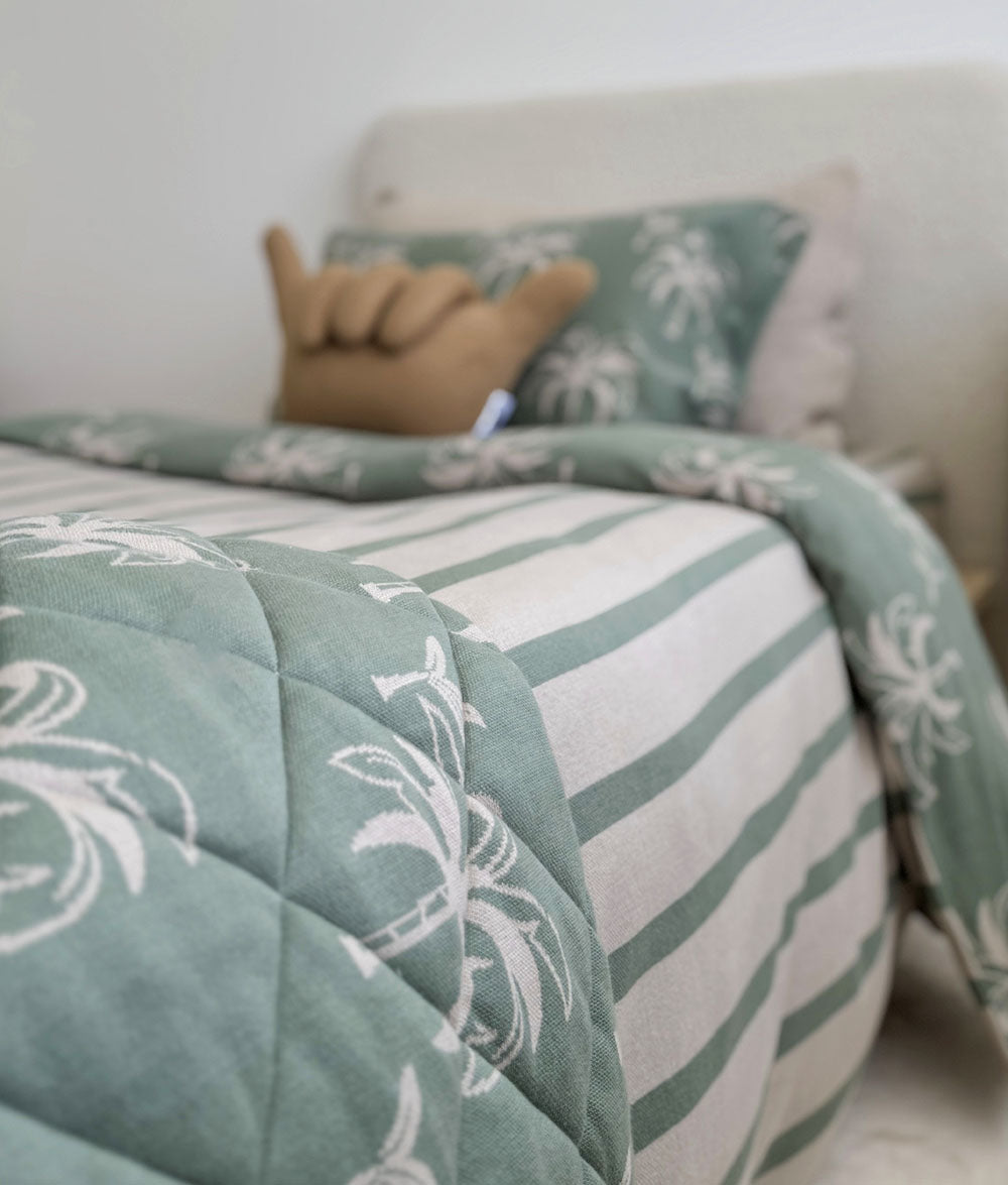 Green and white patterned quilt on a bed with pillows in a bedroom setting.