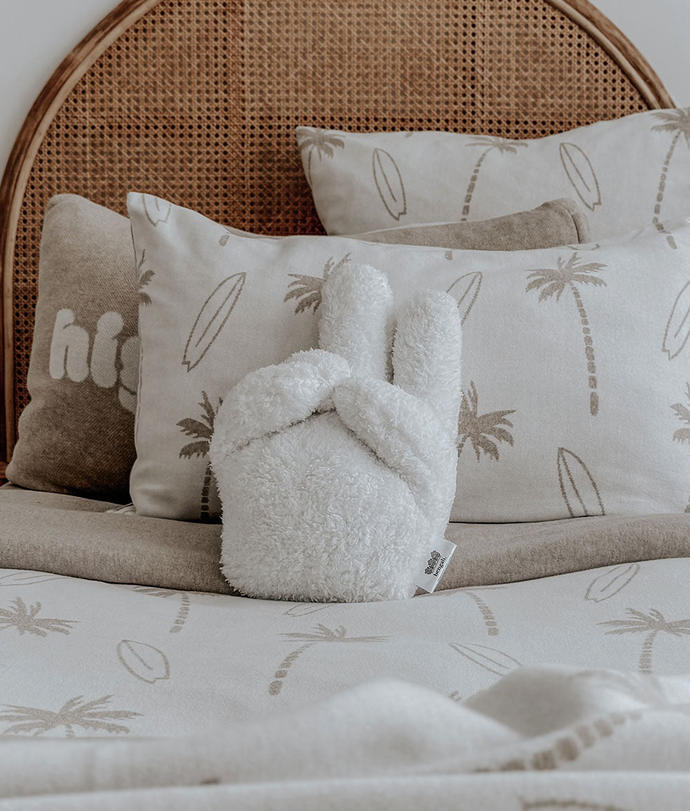 Fluffy white peace cushion on a bed with palm tree patterned pillows and bedding.