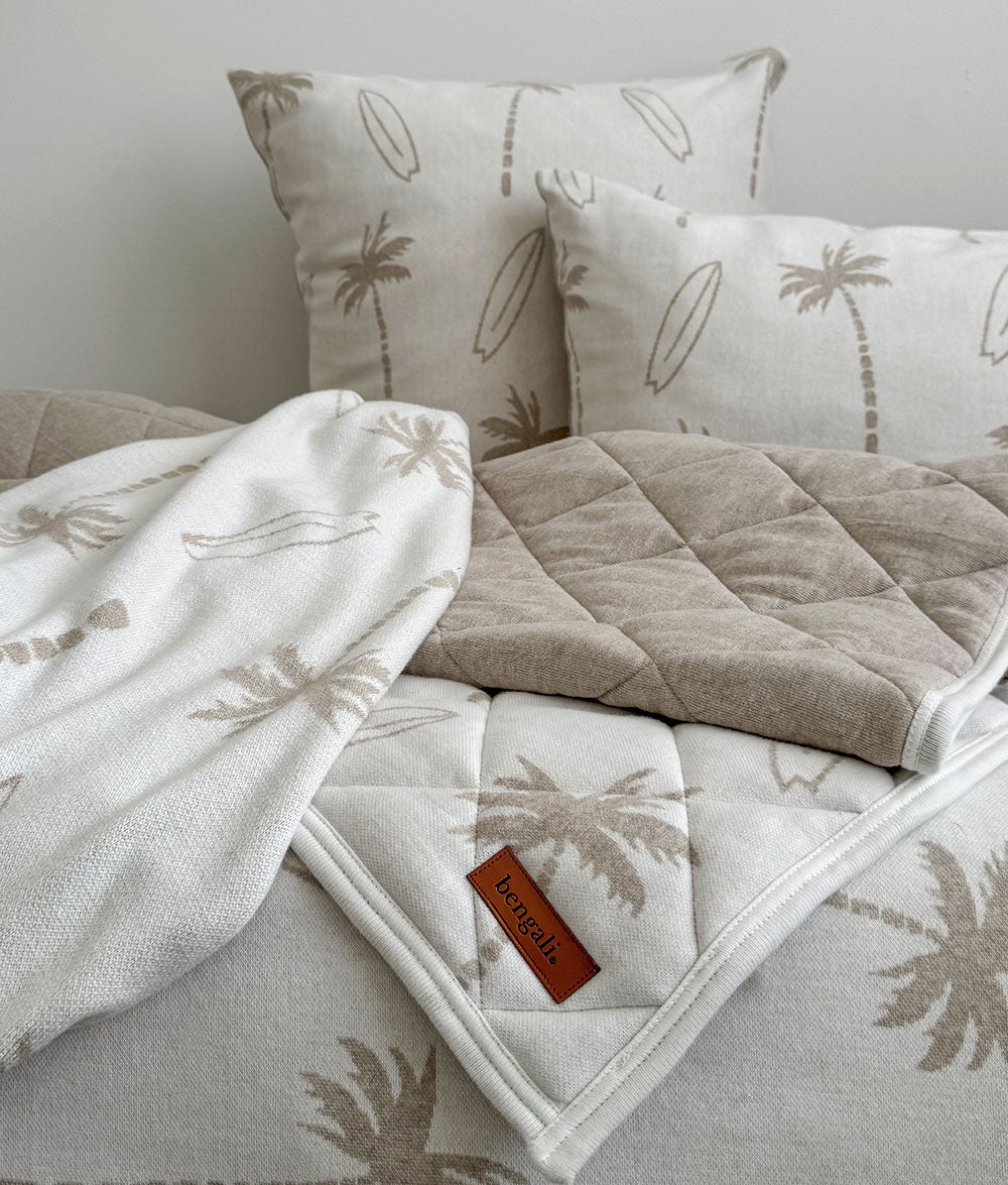 Beige and white bedding set with palm tree patterns on a bed.