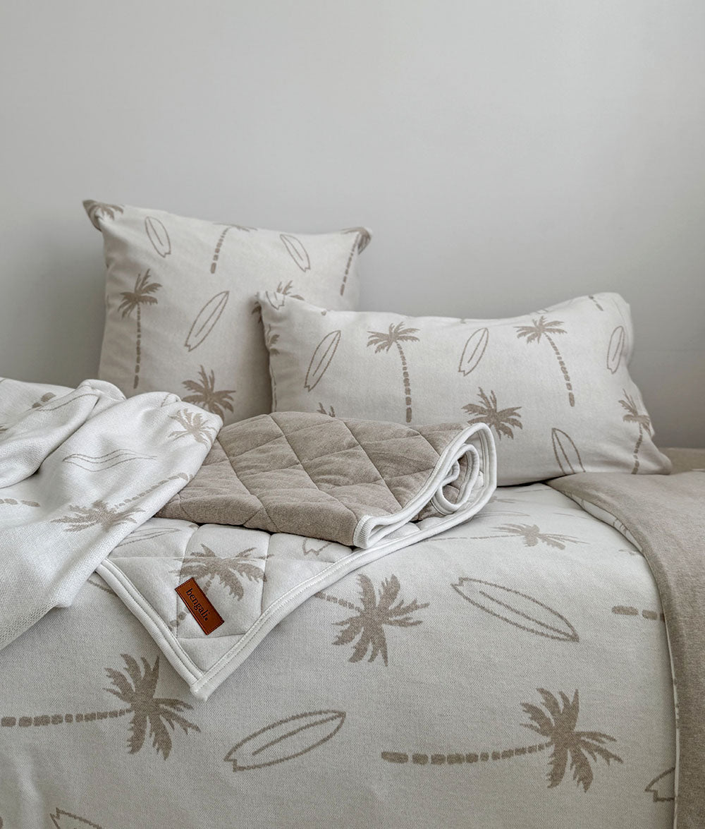Neatly arranged bed with beige and white bedding featuring palm tree patterns.