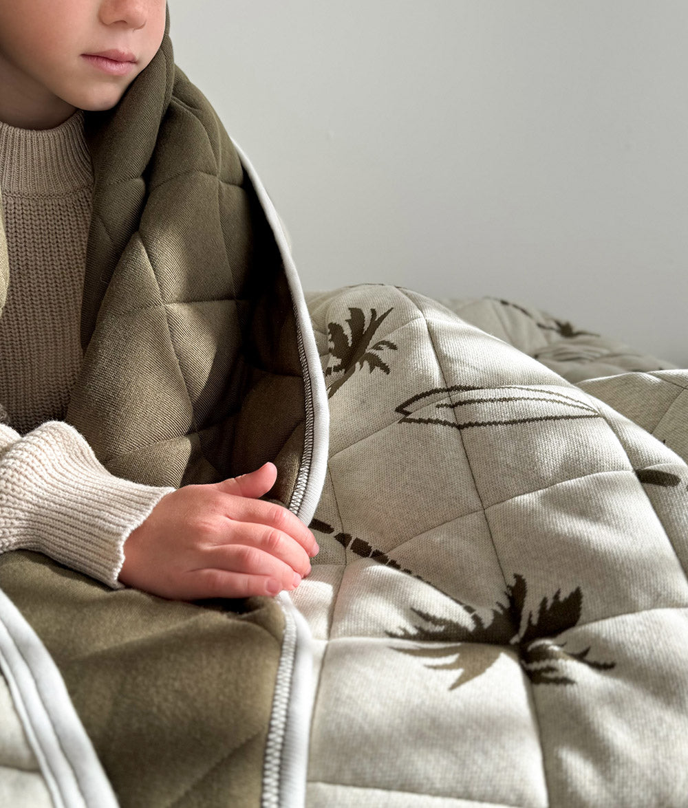 Child wrapped in Olive Surfing Palm jersey cotton quilt.