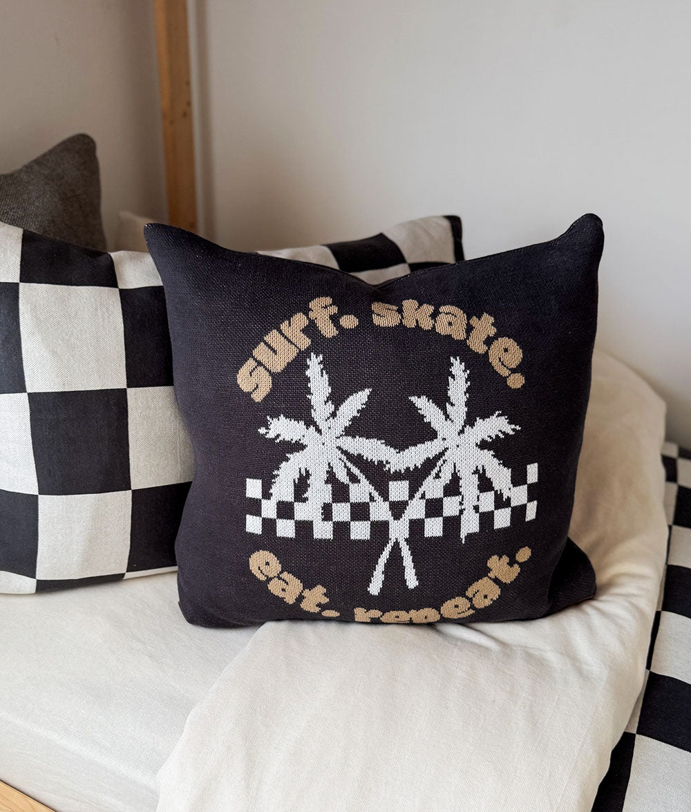 Decorative pillow with text and palm tree design on a couch with checkered cushions.