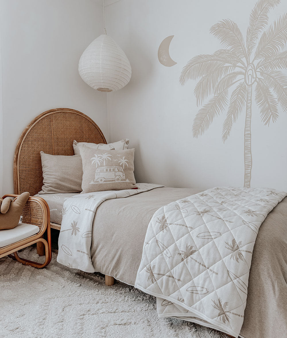 Neatly made bed with decorative pillows and a quilt in a bedroom with a palm tree wall decal.