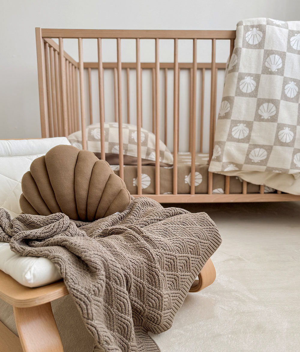 Nursery with wooden crib, shell-shaped pillow, and textured blanket.