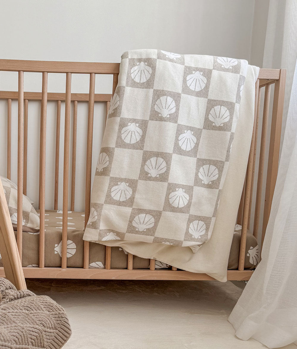 Nursery crib with a shell-patterned blanket draped over it
