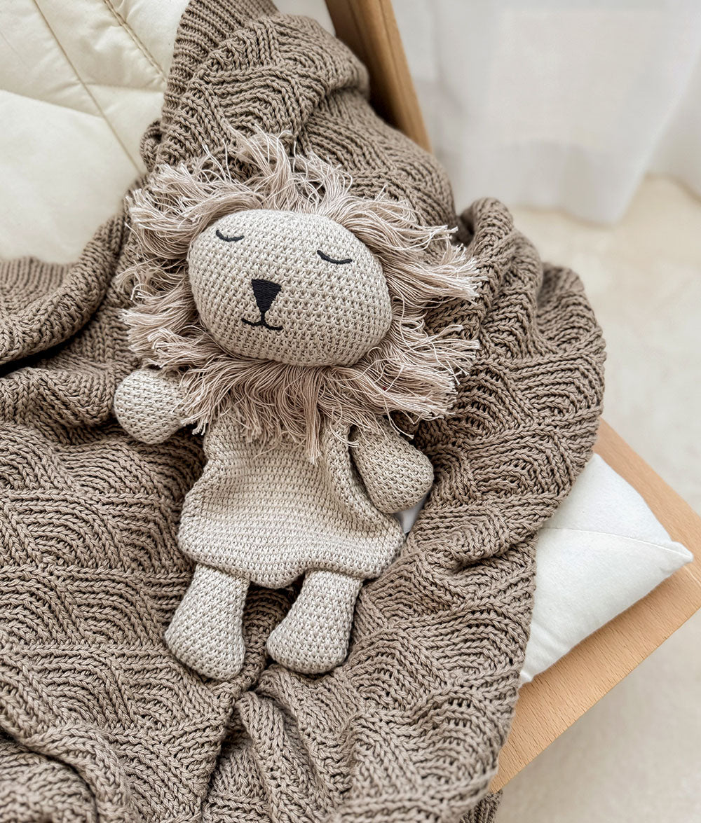 Knitted lion toy on a textured blanket