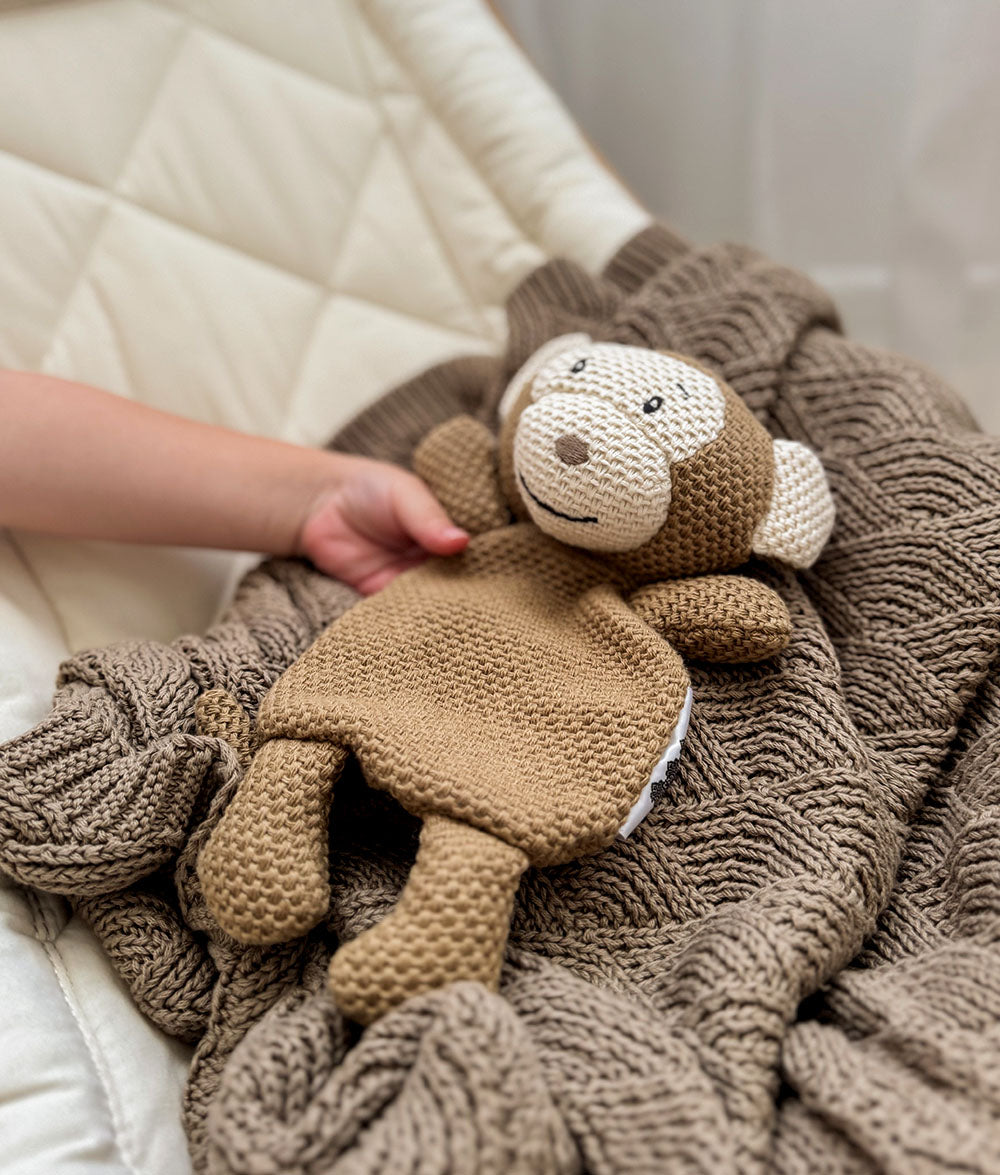 Knitted monkey toy held by a hand on a textured blanket