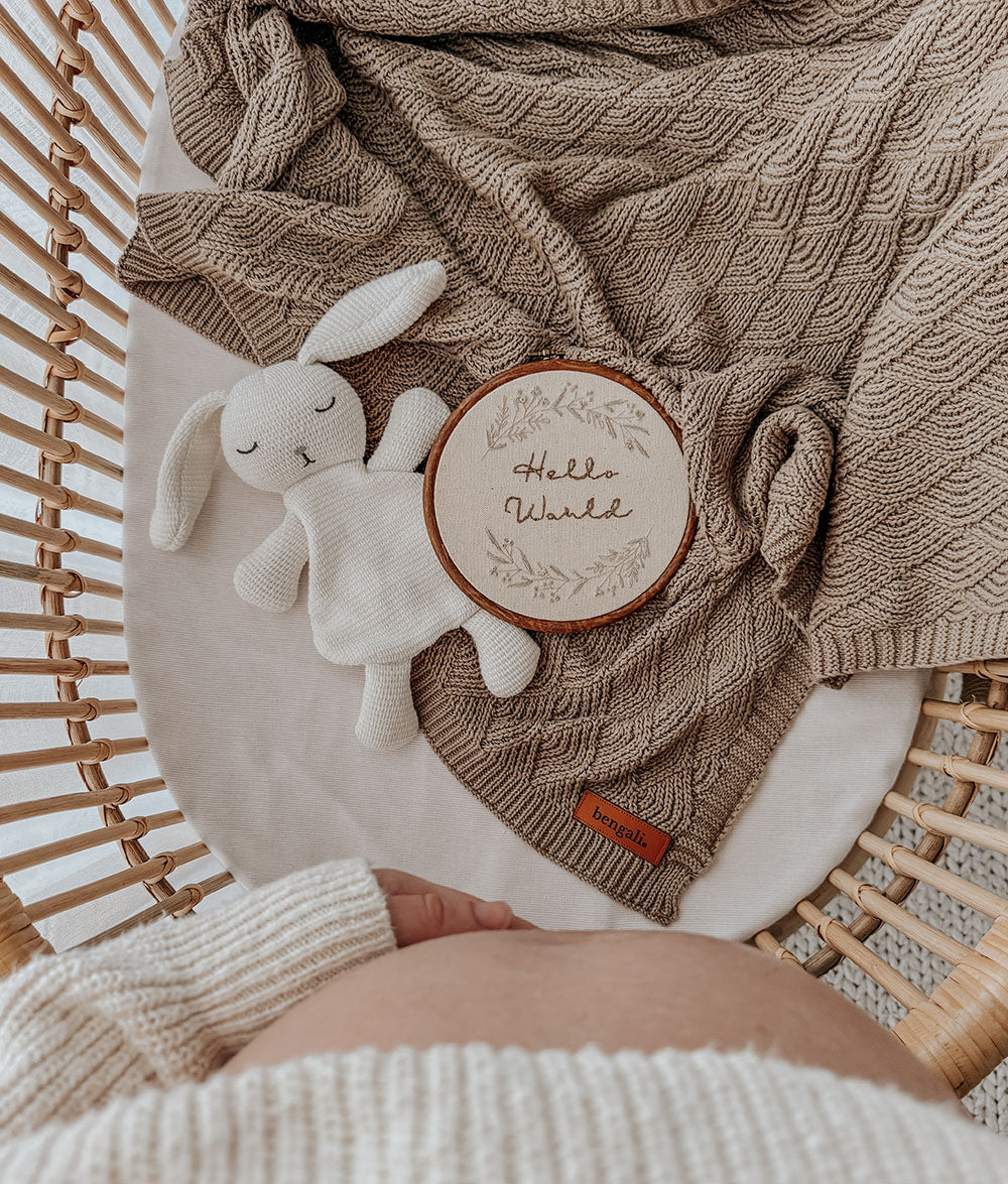 Baby blanket with soft toy and 'Hello World' embroidery on a rattan crib