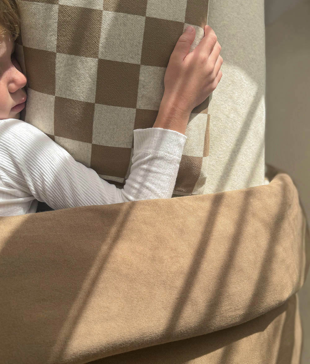 Child hugging the Khaki Gingham pillow while resting under the matching duvet cover.