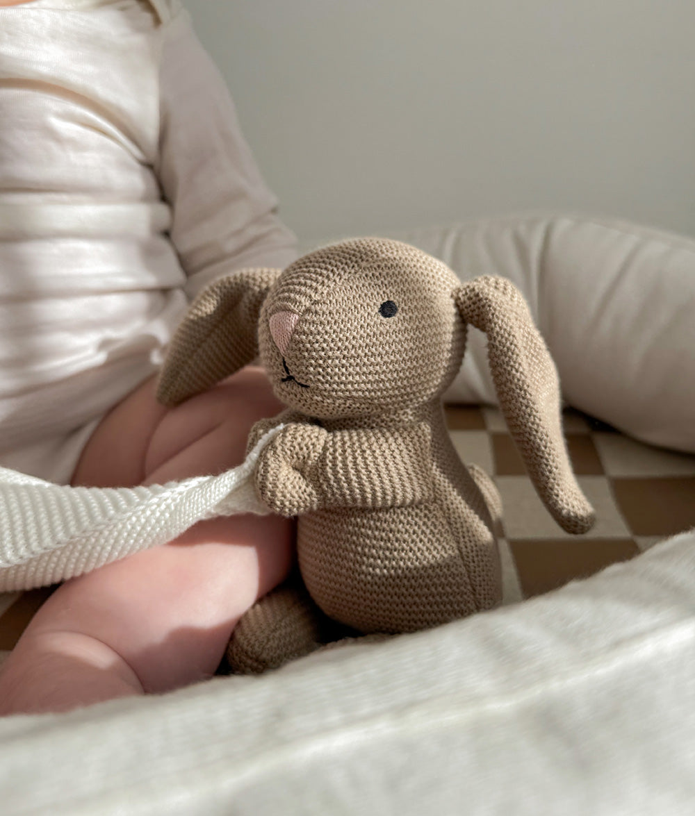 Knitted bunny toy styled in a baby lounger with a chunky check fitted sheet and soft ivory knit blanket.