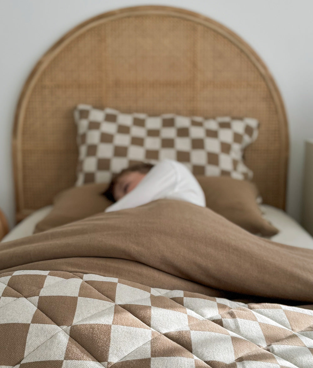 Child resting beneath the Khaki Gingham quilt in a calm, sunlit bedroom.