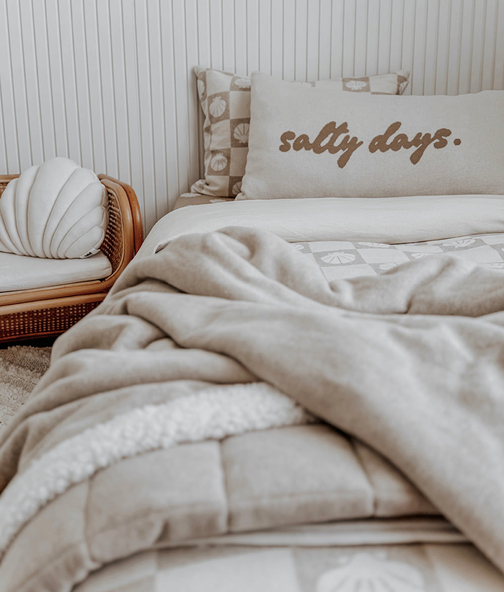 Beige comforter with 'salty days' text on a bed in a bedroom setting.