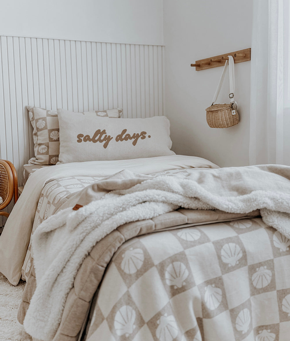 Neatly made bed with 'salty days' pillow and shell-patterned blanket in a bedroom setting.