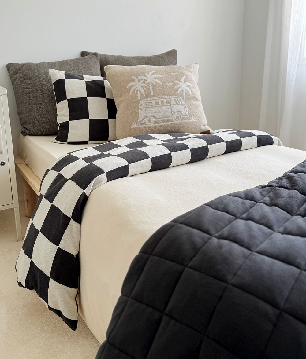 Bed with checkered blanket, gray comforter, and decorative pillows in a bedroom setting.
