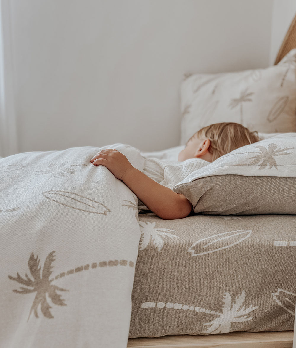 Person lying in bed with patterned bedding featuring palm trees