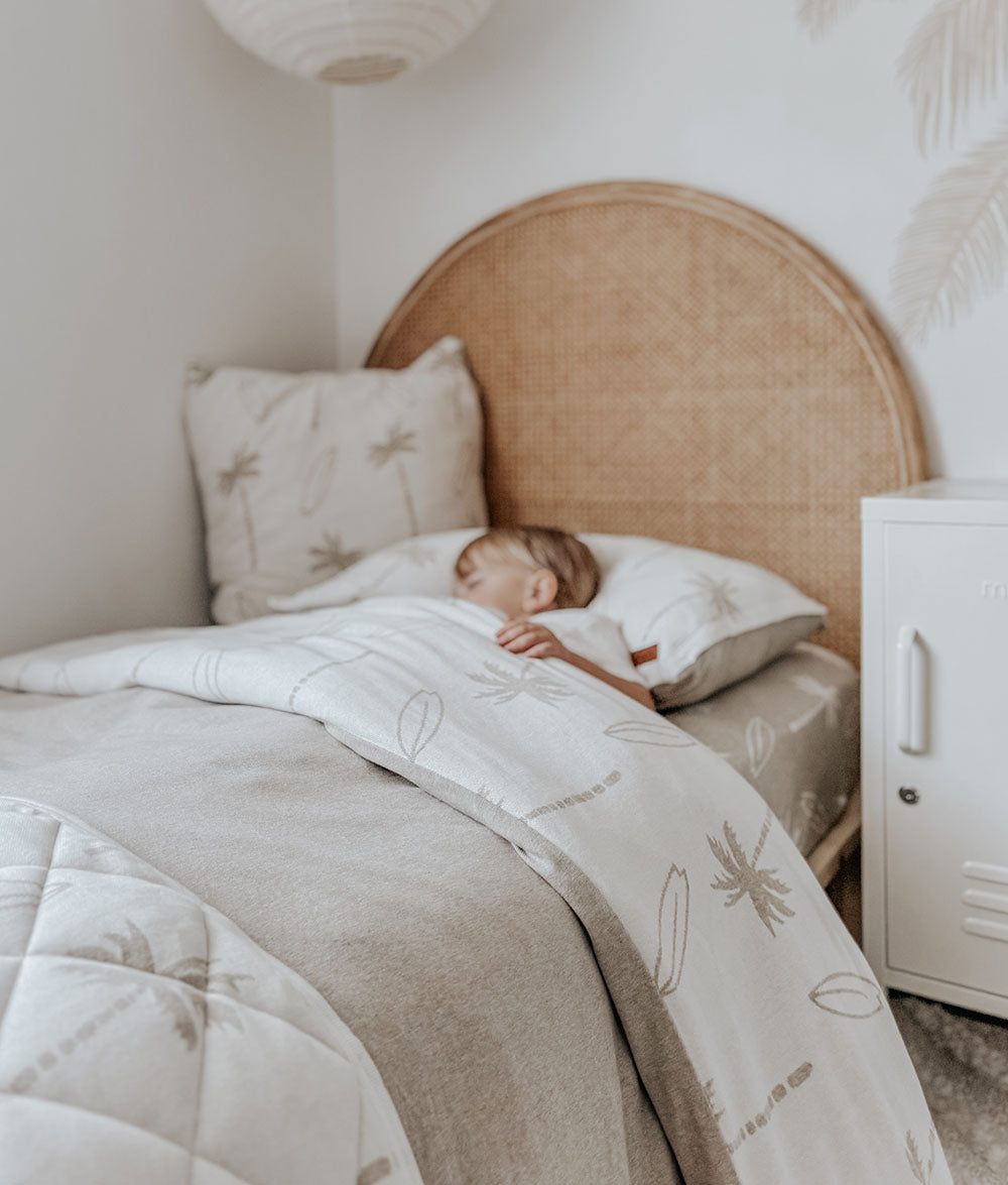 Child sleeping in a bed with a wicker headboard and white bedding.