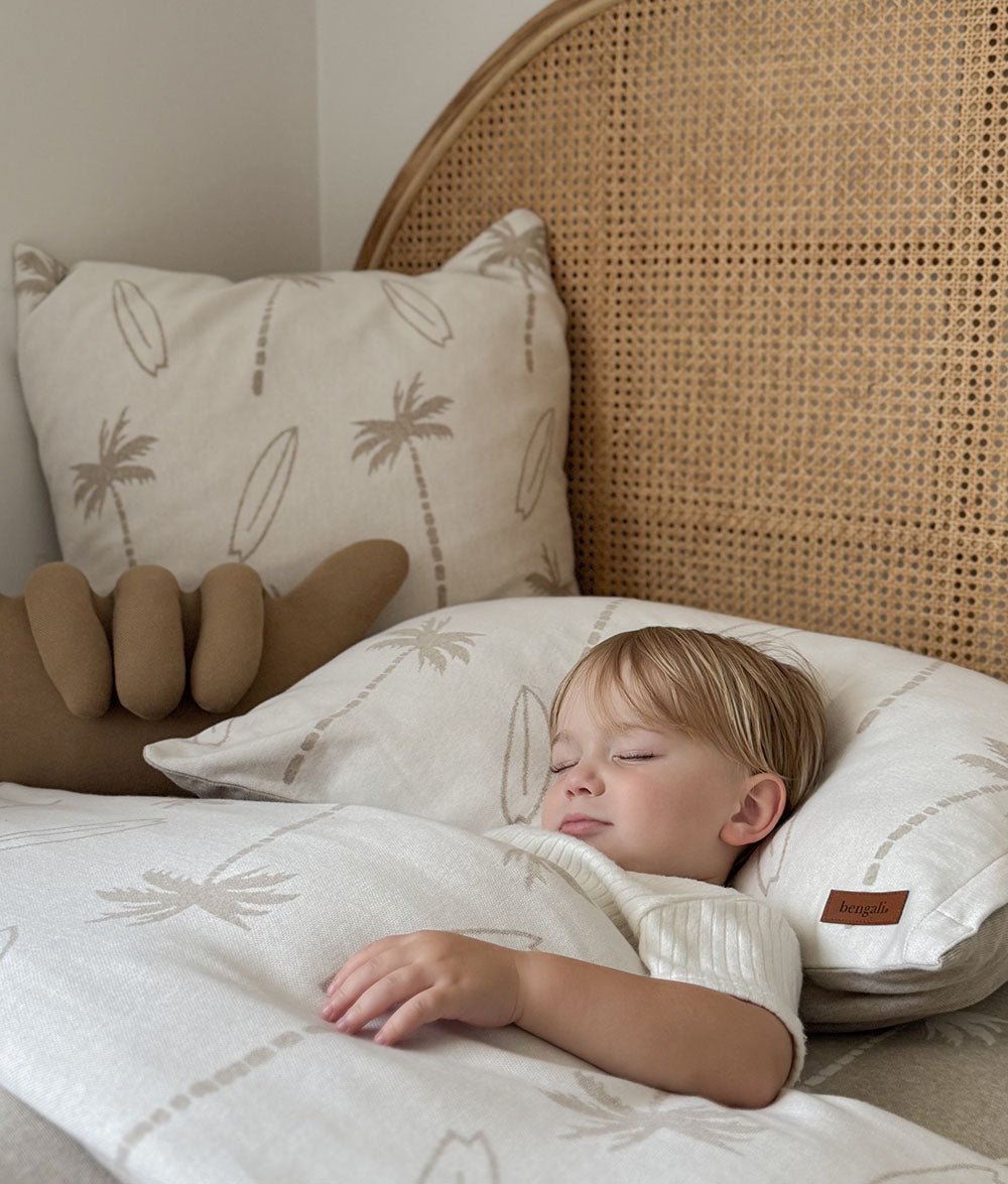 Child sleeping in a bed with palm tree patterned pillows and bedding.