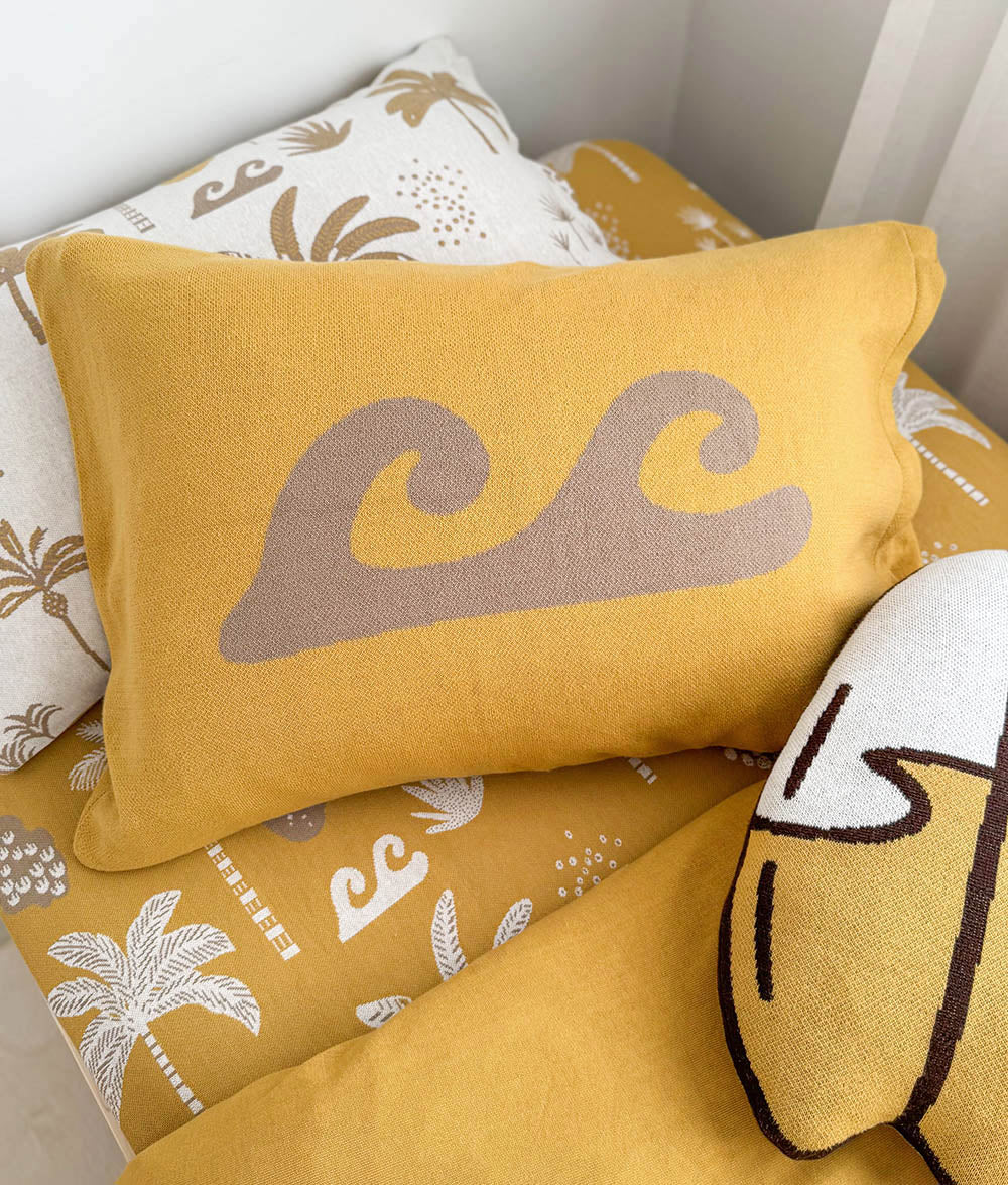 A yellow rectangular throw pillow with a large taupe wave motif, resting on a matching yellow and white patterned cushion set.
