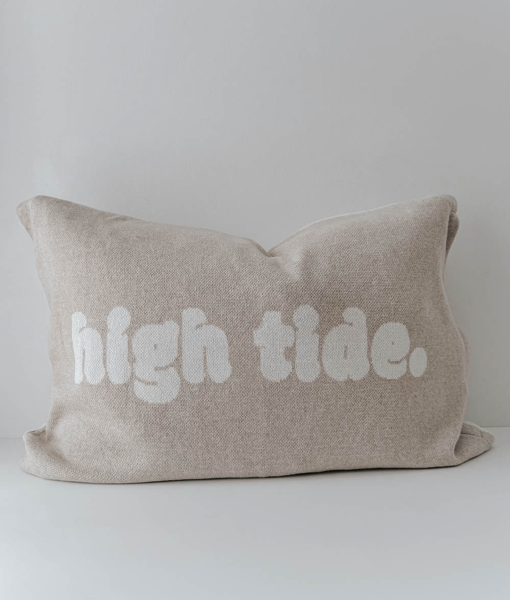 Beige pillow with 'high tide.' text on a light gray background
