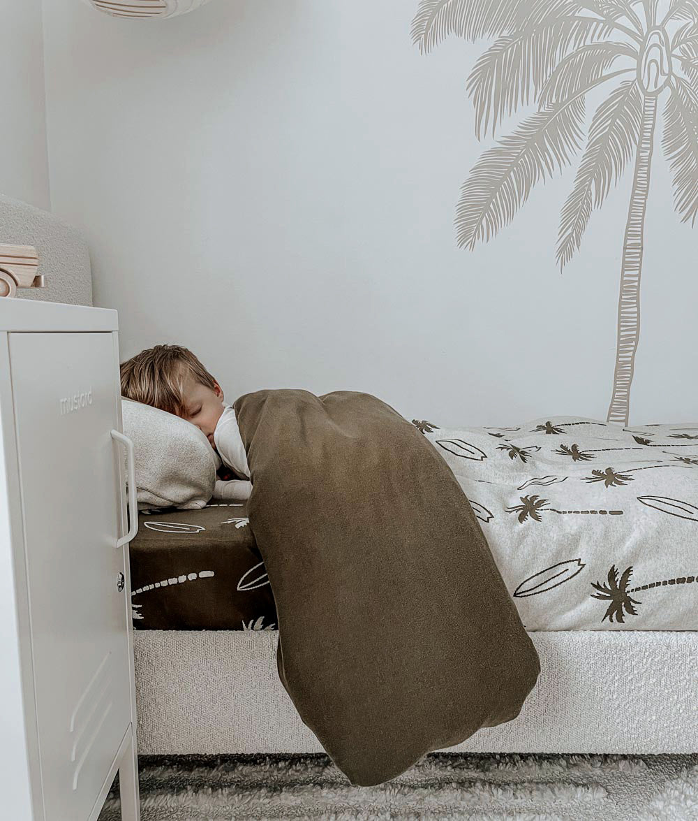 Child sleeping in Olive Surfing Palm jersey cotton bedding.