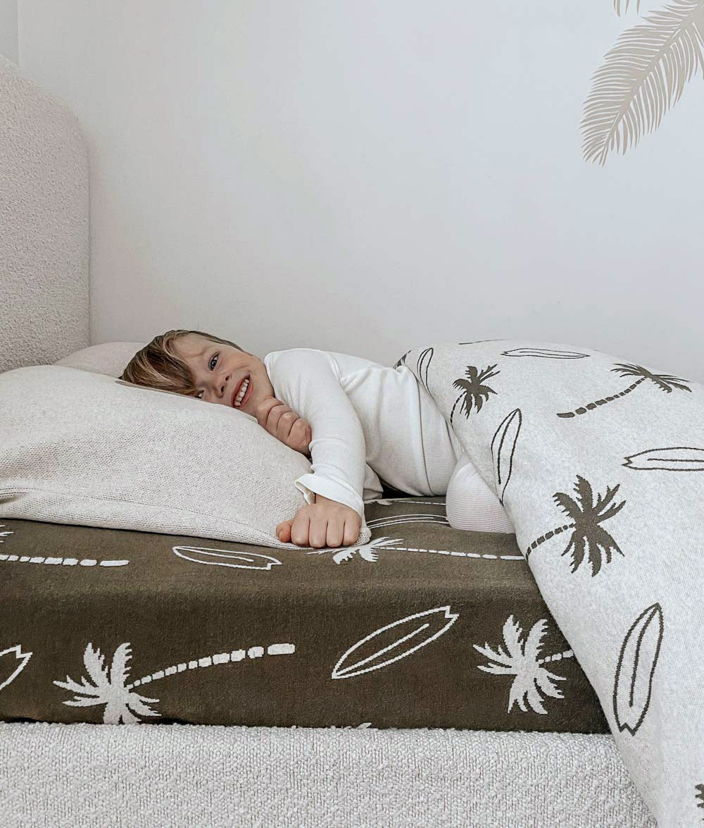 Child relaxing on Olive Surfing Palm jersey cotton fitted sheet.