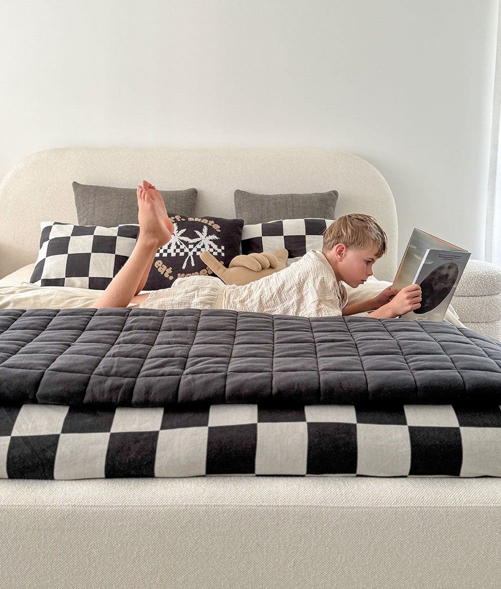 Child lying on a bed with a blanket, reading a book