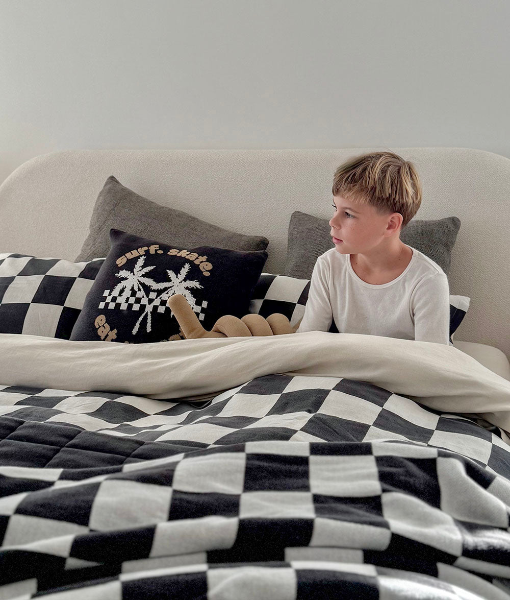 Child sitting on a bed with checkered blanket and pillows