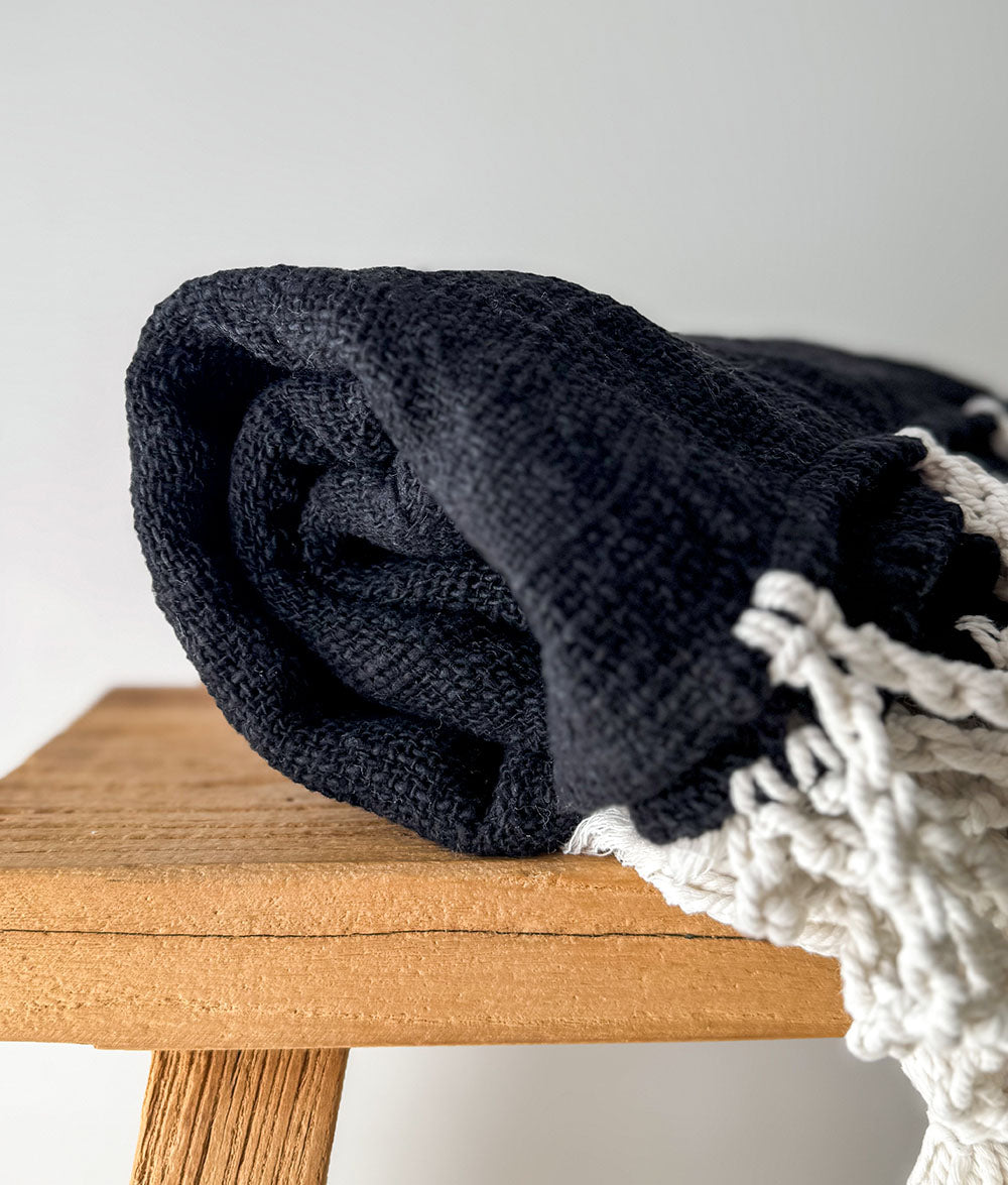 Rolled-up black blanket on a wooden surface with a white background