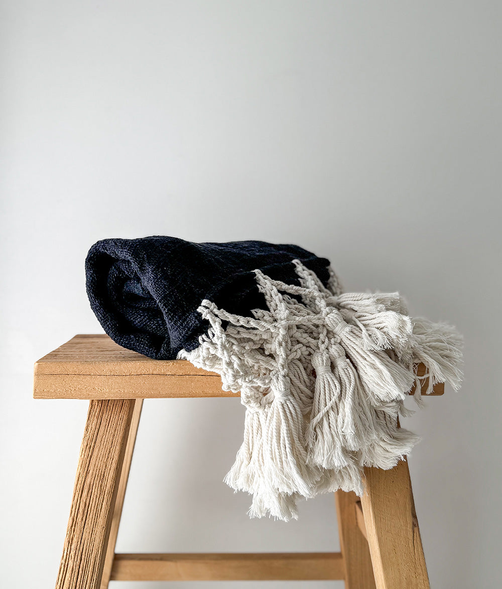Black and white textured blanket draped over a wooden stool against a plain background