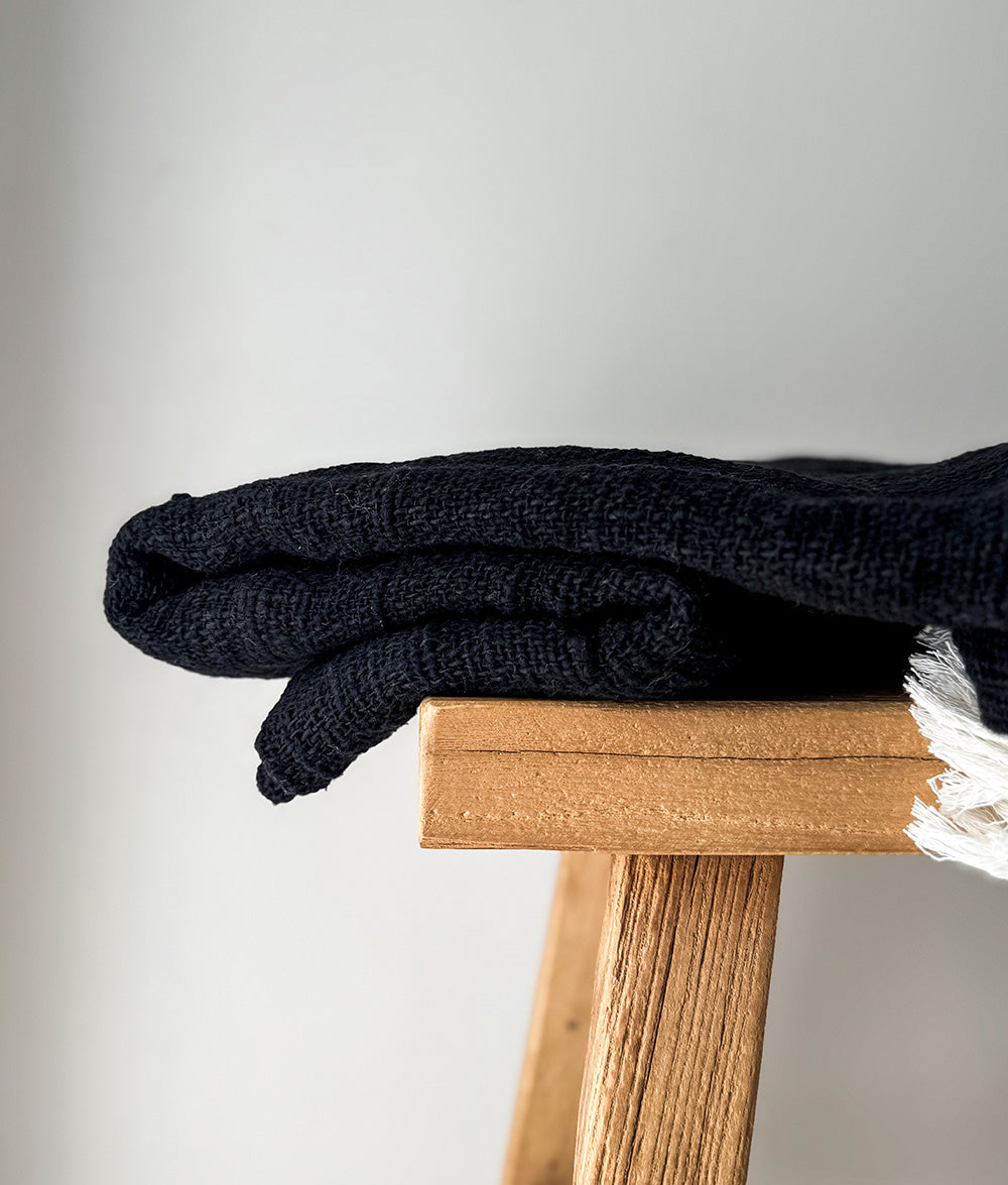 Black knit blanket on a wooden stool against a light gray background