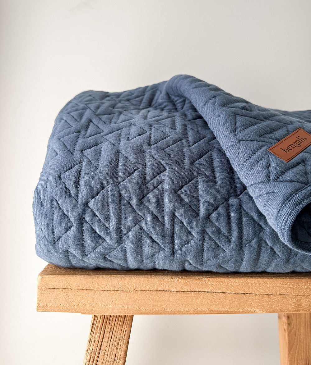 Blue quilted blanket on a wooden stool with a neutral background