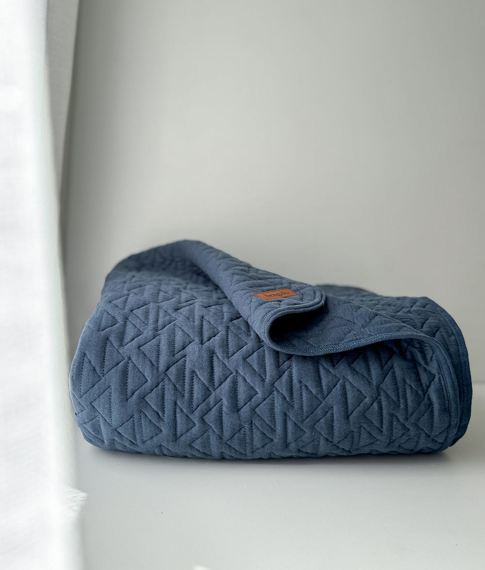 Blue quilted blanket on a white surface with a light gray background