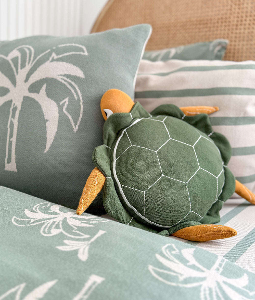 Green turtle plush toy on a cushion with palm tree patterns