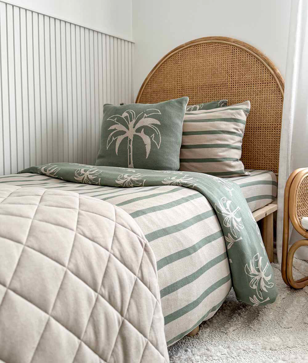 Bed with green and beige striped bedding, palm tree pillow, and wicker headboard.