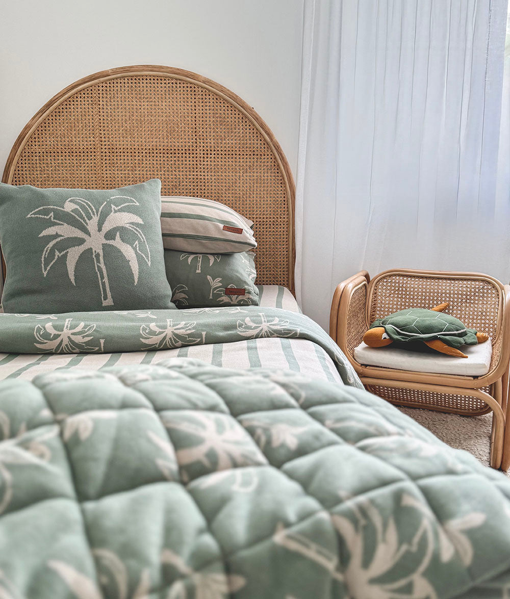 Bed with wicker headboard and matching chair, featuring palm tree design on bedding.