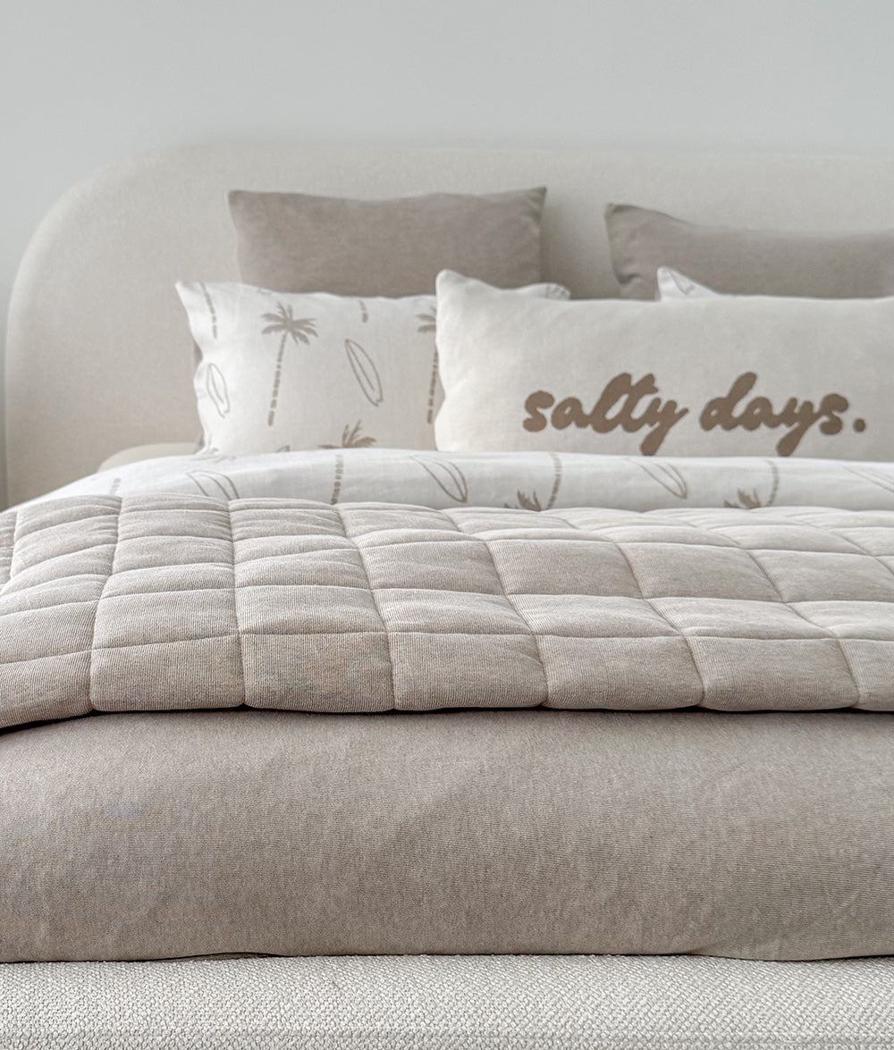Beige comforter with 'salty days' text on a bed with decorative pillows.