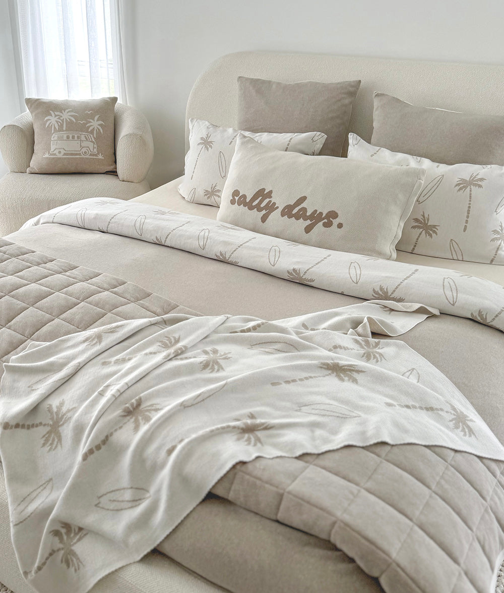 Neatly made bed with decorative pillows and a blanket in a bedroom setting.