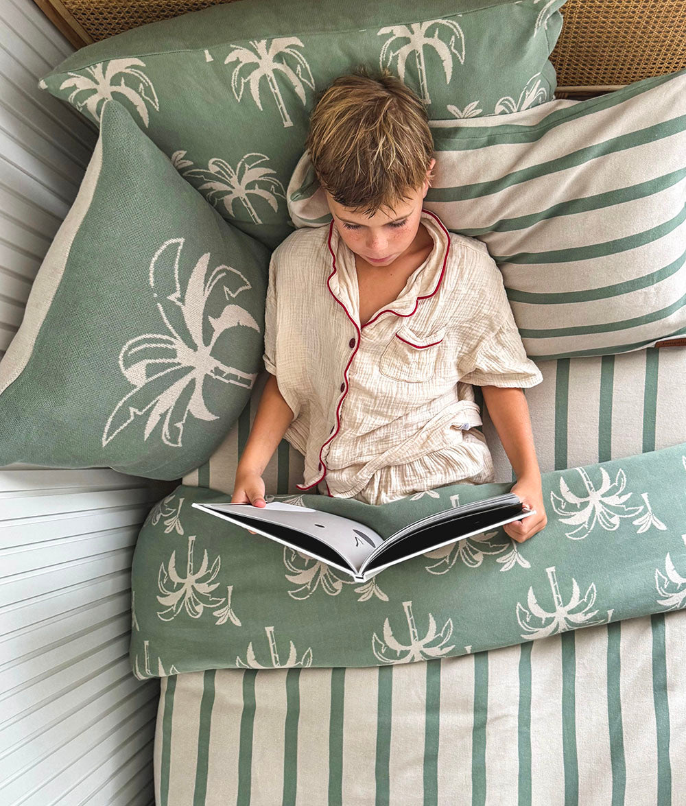 Child reading a book on a bed with green and beige palm tree patterned pillows