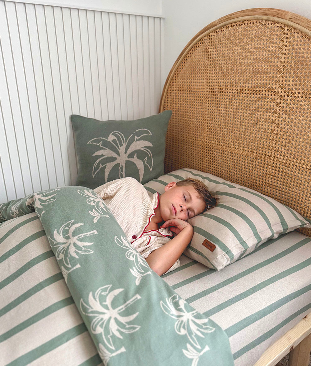 Child sleeping on a bed with palm tree patterned bedding and pillows.